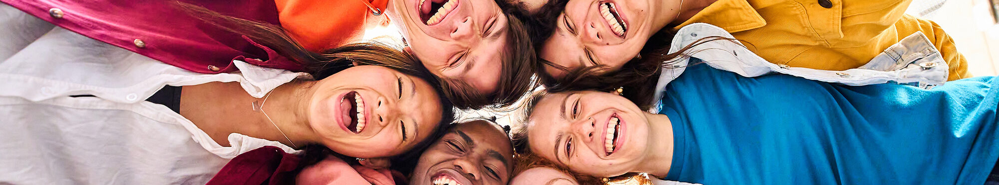 Large multiracial group of smiling young people standing hugging looking at camera. Low angle view.